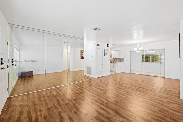 unfurnished living room with baseboards, a notable chandelier, visible vents, and wood finished floors