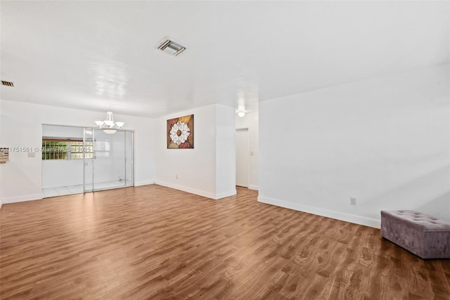 unfurnished living room with a chandelier, visible vents, and wood finished floors