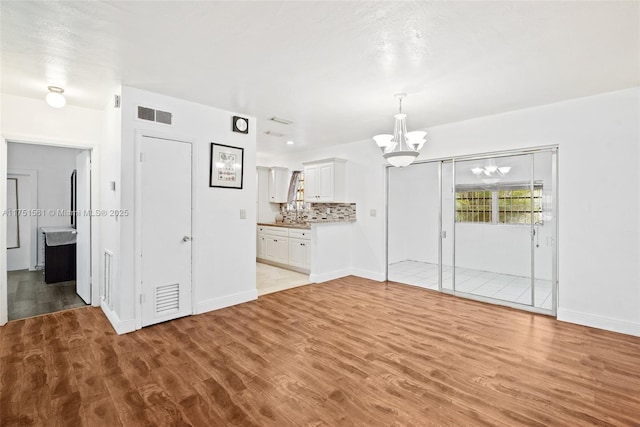 unfurnished living room featuring light wood-type flooring, baseboards, visible vents, and a notable chandelier