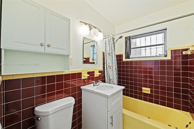 full bath featuring toilet, a wainscoted wall, shower / bath combination with curtain, vanity, and tile walls