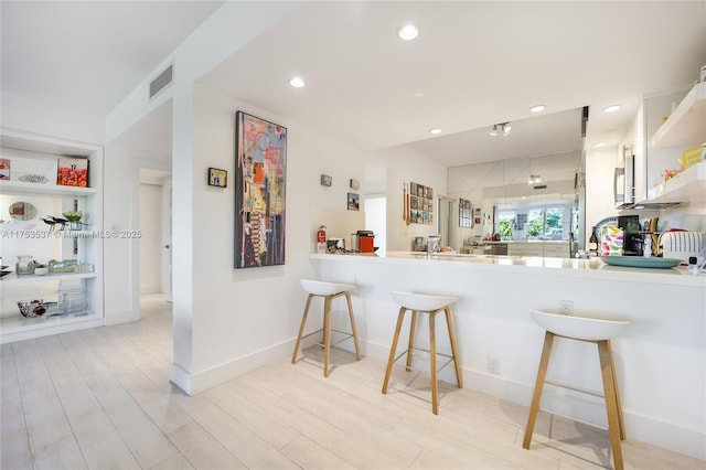 kitchen with open shelves, visible vents, stainless steel microwave, light wood-style flooring, and a kitchen bar