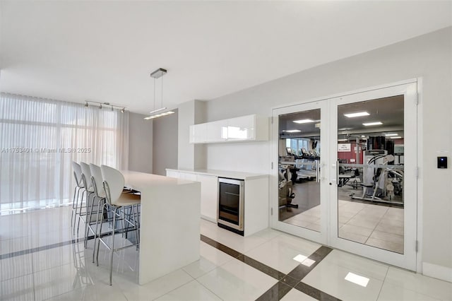 kitchen with wine cooler, a kitchen breakfast bar, french doors, white cabinetry, and light tile patterned flooring