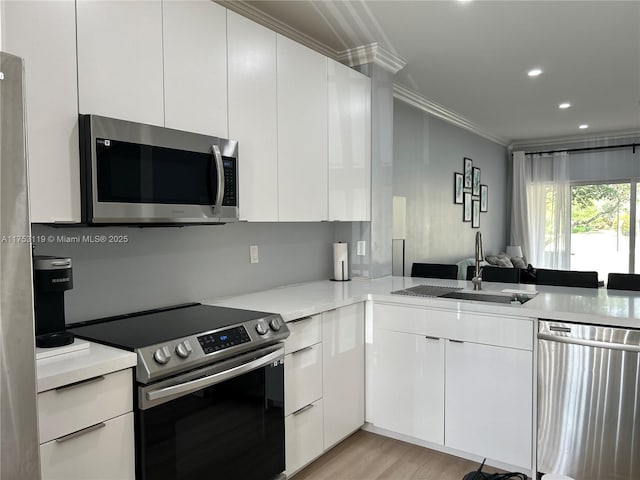 kitchen with ornamental molding, appliances with stainless steel finishes, a sink, and white cabinetry