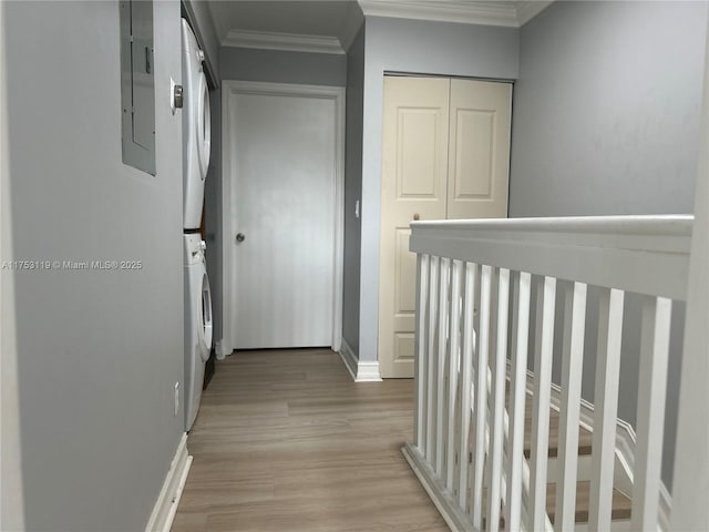 hall featuring light wood finished floors, electric panel, baseboards, stacked washer and clothes dryer, and crown molding