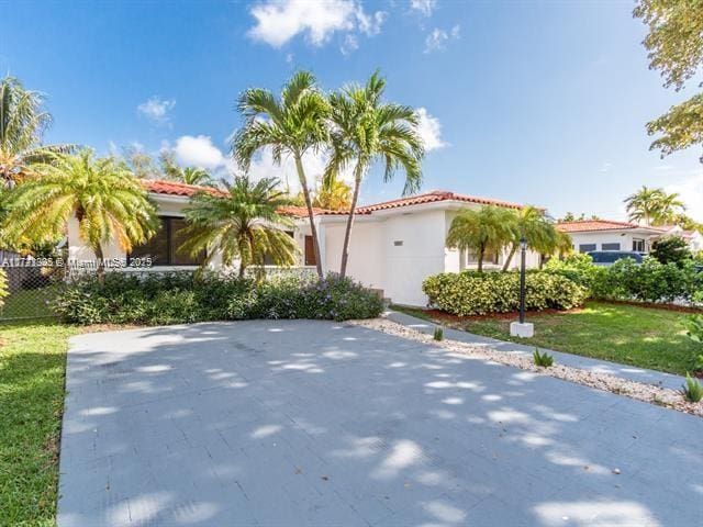 mediterranean / spanish house with a front yard, a tile roof, fence, and stucco siding