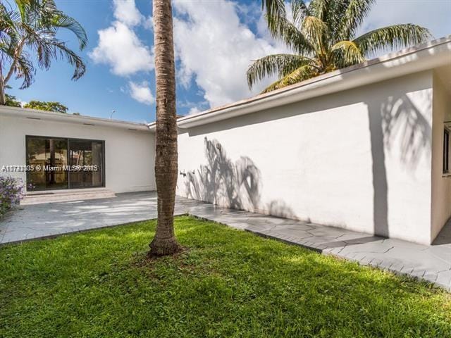 rear view of property featuring a patio, a lawn, and stucco siding