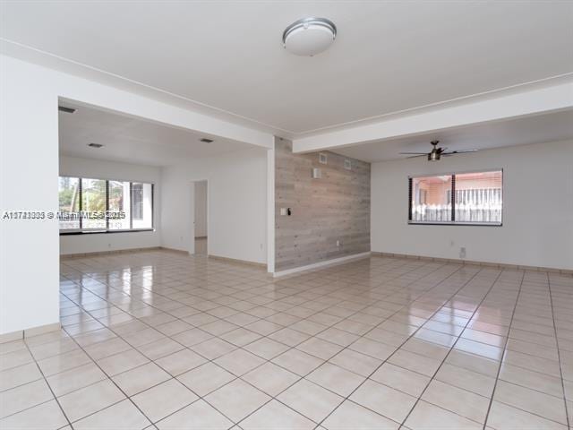 spare room featuring light tile patterned floors, wooden walls, baseboards, ceiling fan, and beam ceiling