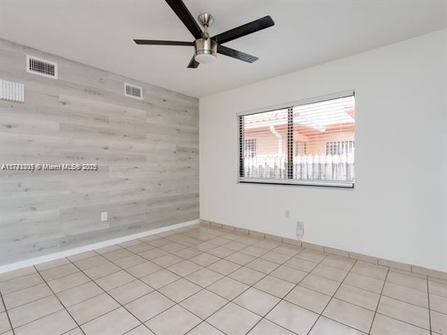 empty room with light tile patterned floors, wood walls, visible vents, and a ceiling fan