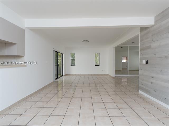 spare room featuring wood walls, baseboards, beamed ceiling, and light tile patterned flooring