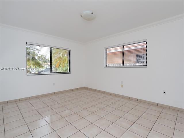 spare room with baseboards, ornamental molding, and light tile patterned flooring