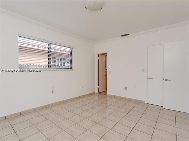 spare room featuring light tile patterned floors, ornamental molding, visible vents, and baseboards