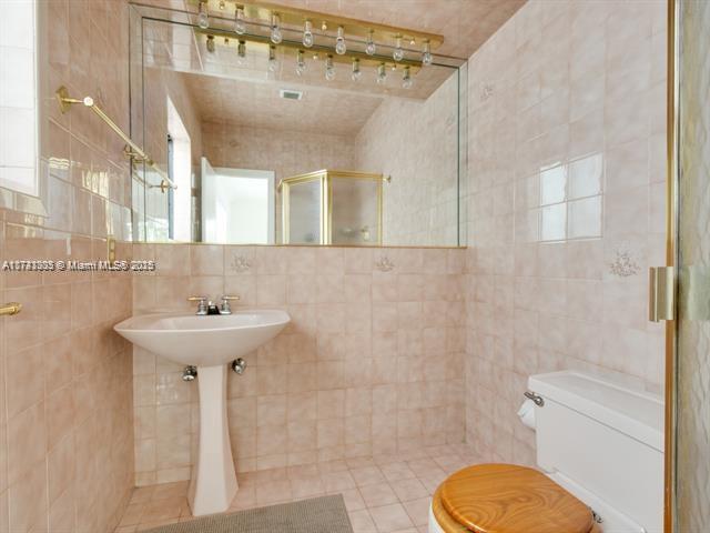 bathroom featuring toilet, a stall shower, tile walls, and tile patterned floors