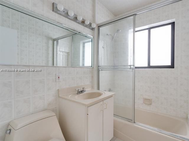 full bathroom with vanity, tile walls, toilet, and bath / shower combo with glass door