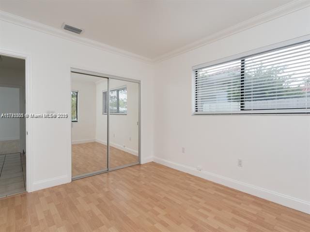 unfurnished bedroom with ornamental molding, light wood-type flooring, a closet, and baseboards