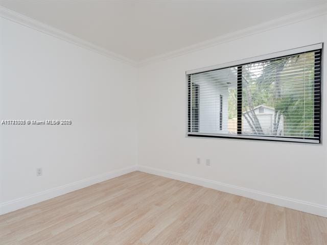 spare room with baseboards, wood finished floors, and crown molding