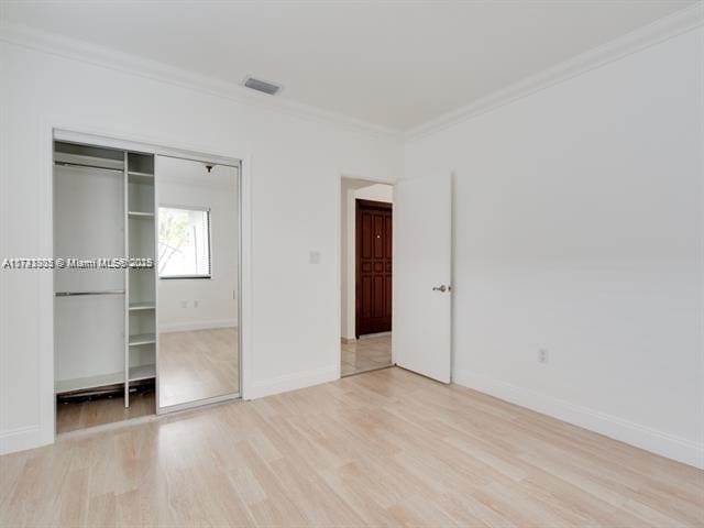 unfurnished bedroom featuring light wood finished floors, visible vents, baseboards, ornamental molding, and a closet