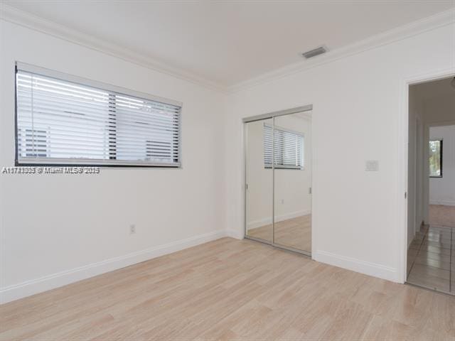 unfurnished bedroom featuring visible vents, baseboards, a closet, light wood finished floors, and crown molding