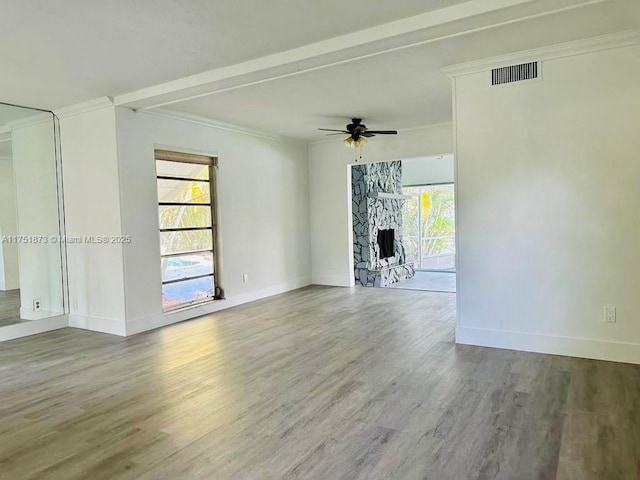 unfurnished room featuring ornamental molding, a stone fireplace, wood finished floors, and visible vents