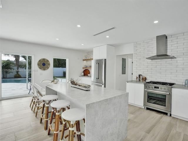 kitchen featuring wall chimney exhaust hood, modern cabinets, stainless steel appliances, a kitchen bar, and white cabinetry