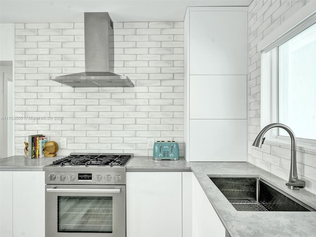 kitchen featuring stainless steel gas range, plenty of natural light, a sink, and wall chimney range hood