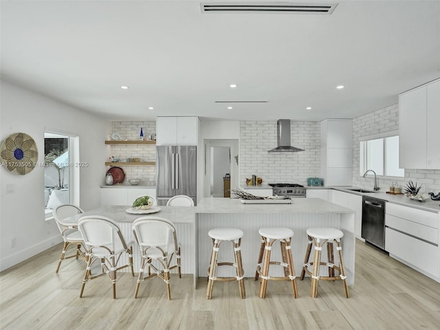 kitchen featuring white cabinets, modern cabinets, appliances with stainless steel finishes, wall chimney range hood, and a sink