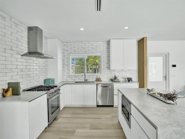 kitchen featuring wall chimney exhaust hood, appliances with stainless steel finishes, a sink, and white cabinetry