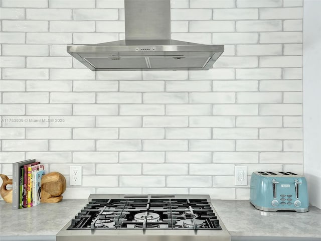 room details featuring decorative backsplash, cooktop, light countertops, and wall chimney exhaust hood