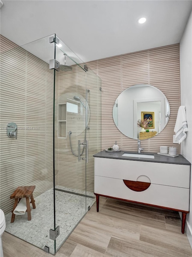 full bath with toilet, a stall shower, vanity, and tile walls