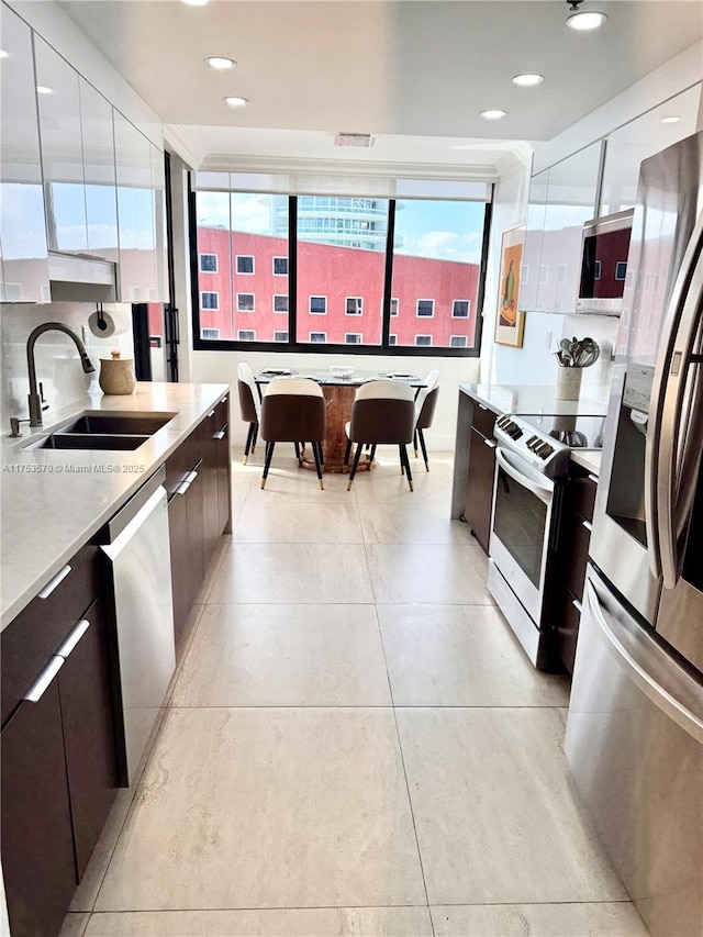kitchen with a sink, appliances with stainless steel finishes, light countertops, dark brown cabinetry, and modern cabinets