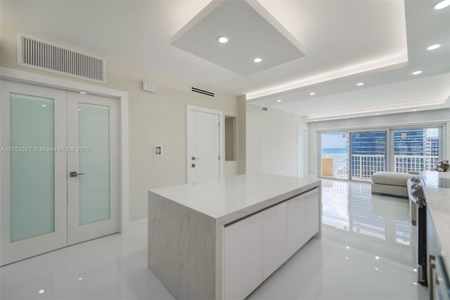 kitchen featuring a center island, a raised ceiling, visible vents, white cabinetry, and modern cabinets