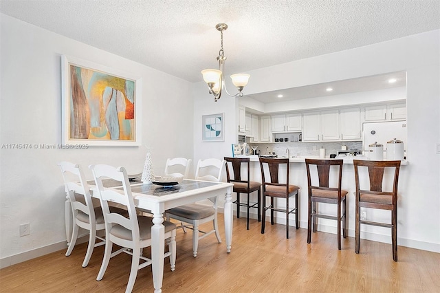 dining space with recessed lighting, an inviting chandelier, light wood-style floors, a textured ceiling, and baseboards