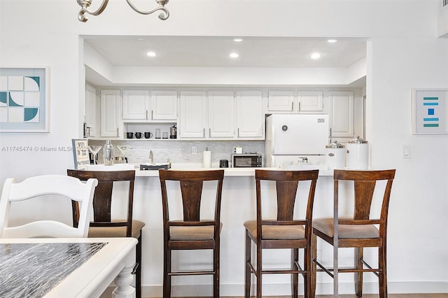 kitchen featuring tasteful backsplash, a kitchen breakfast bar, freestanding refrigerator, light countertops, and white cabinetry