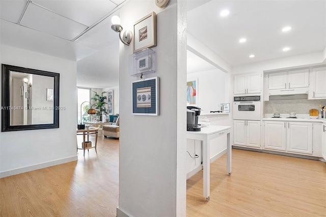 kitchen featuring light countertops, light wood-style flooring, white cabinetry, white appliances, and under cabinet range hood