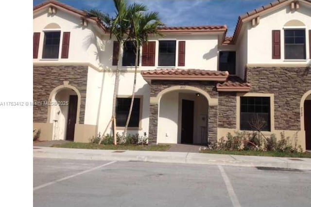 mediterranean / spanish-style house featuring stone siding, a tiled roof, and stucco siding