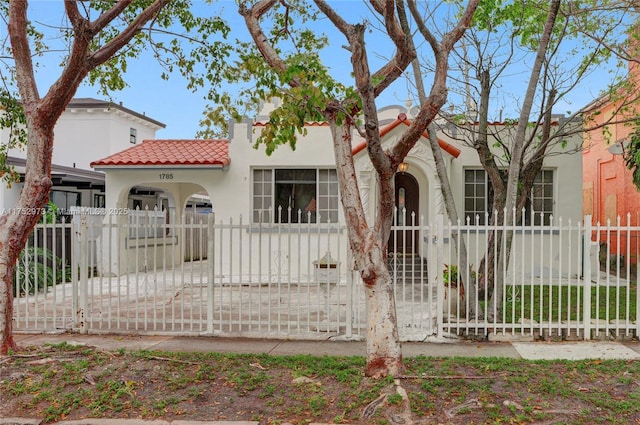 mediterranean / spanish-style house with a fenced front yard, a tiled roof, and stucco siding