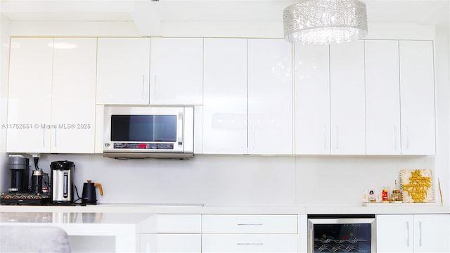 kitchen featuring light countertops, stainless steel microwave, white cabinets, modern cabinets, and beverage cooler