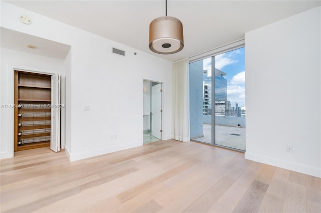 spare room featuring expansive windows, visible vents, light wood-style flooring, and baseboards