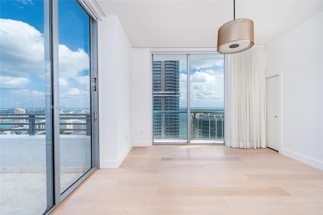 unfurnished room featuring baseboards, a view of city, wood finished floors, and floor to ceiling windows