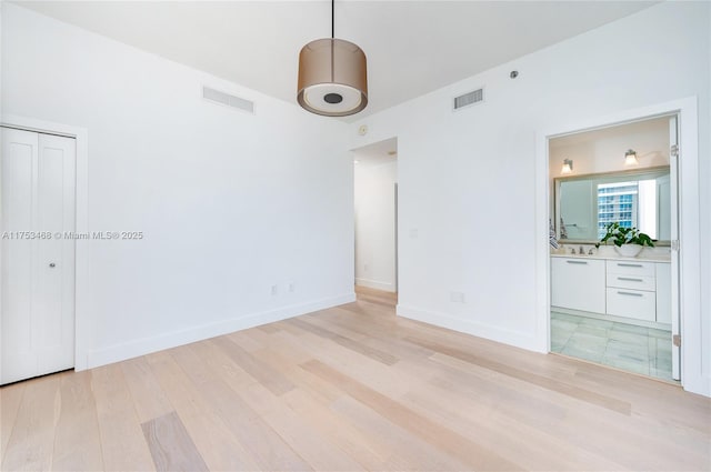 empty room featuring light wood-style floors, visible vents, and baseboards