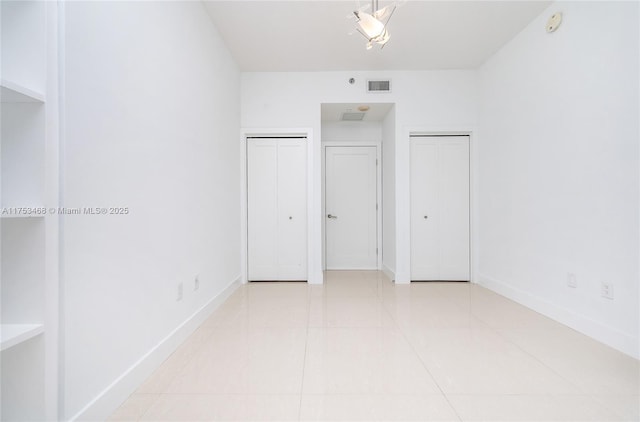 unfurnished bedroom with visible vents, two closets, baseboards, and tile patterned floors