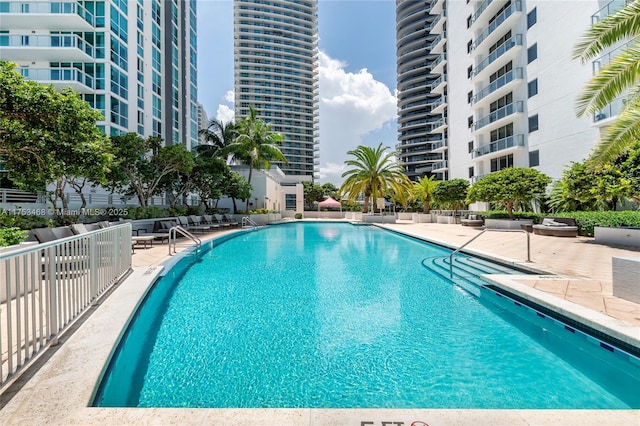 community pool with a patio area, fence, and a city view