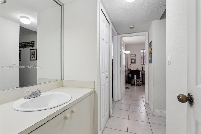 bathroom with a textured ceiling, tile patterned flooring, vanity, and baseboards