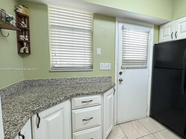 kitchen featuring stone countertops, white cabinets, and freestanding refrigerator