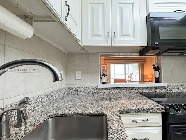 kitchen featuring stone counters, backsplash, white cabinetry, a sink, and black appliances