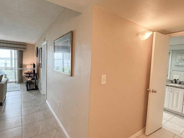 corridor with a sink, a textured ceiling, baseboards, and light tile patterned floors