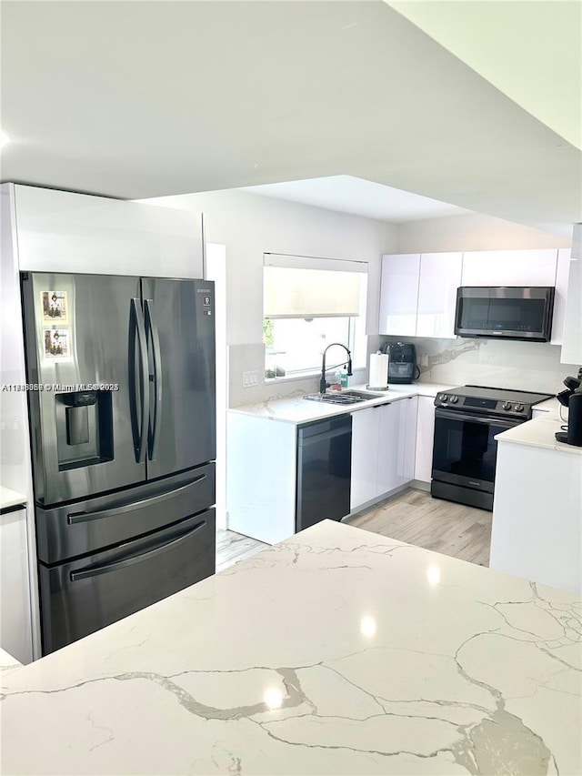 kitchen featuring light stone countertops, appliances with stainless steel finishes, white cabinets, and a sink