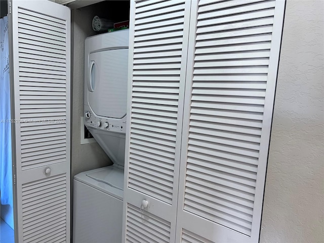 clothes washing area with laundry area, a textured wall, and stacked washing maching and dryer