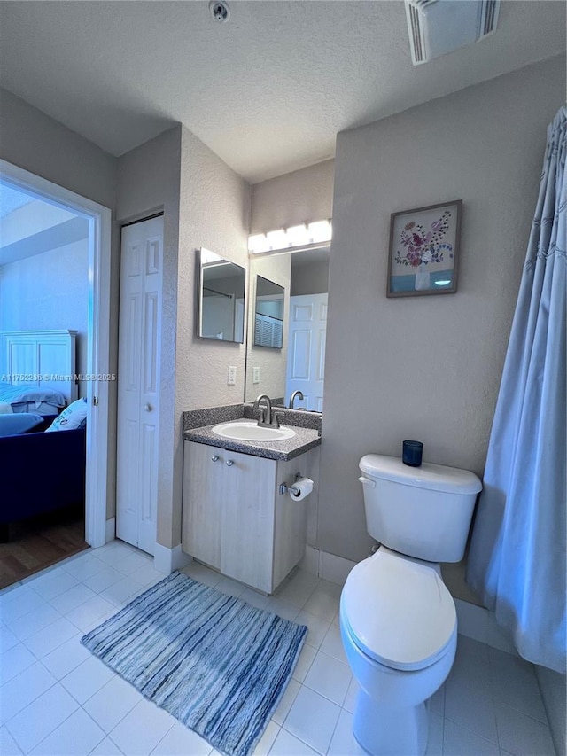 ensuite bathroom with visible vents, toilet, tile patterned flooring, a textured ceiling, and vanity