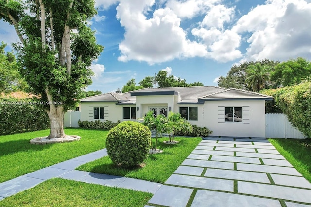 rear view of house featuring stucco siding, a tile roof, fence, and a yard