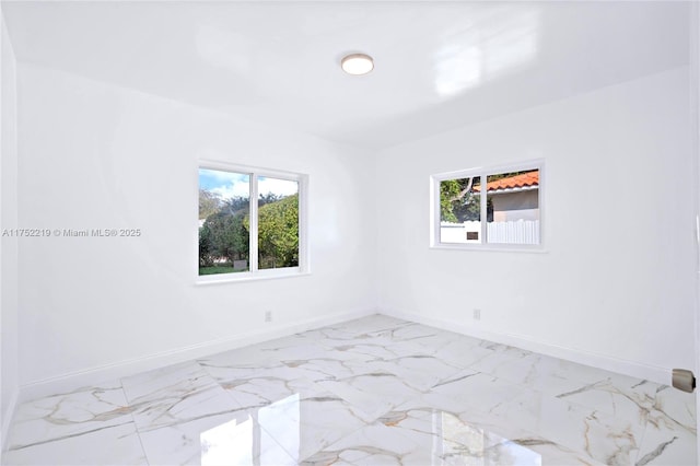 spare room featuring marble finish floor and baseboards